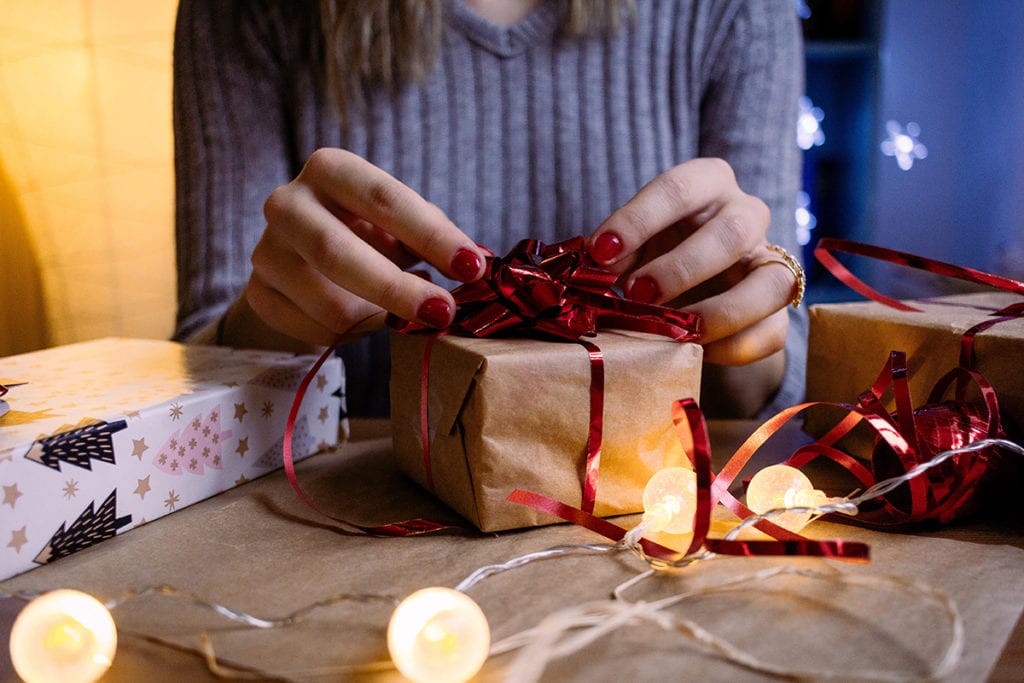 how to give gifts sustainably woman wrapping a present in brown wrapping paper