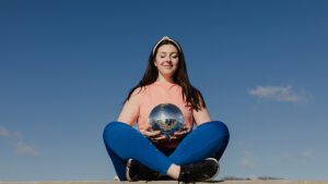 Woman meditating with disco ball in her hands and a blue sky behind her